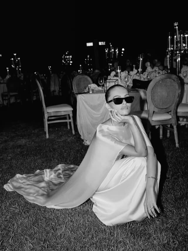 Mariée assise dans l'herbe au dîner, robe satin et cape